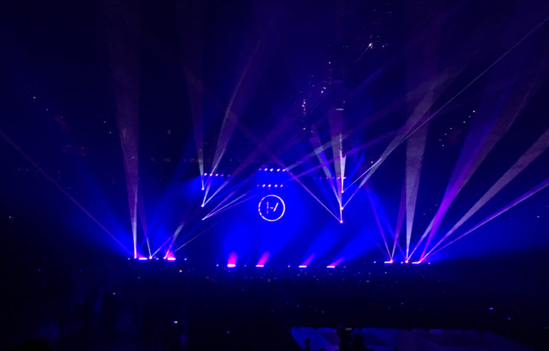 Twenty One Pilots concert with purple lights and the band's logo projected on the back wall of the stage