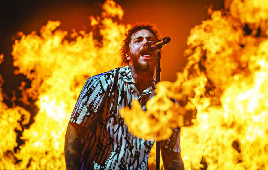 Picture of Post Malone singing with fire surrounding him.